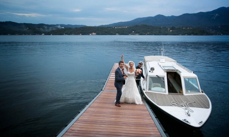 The couple on a jetty beside a wooden motor launch on Lake Orta, by Ustaria Ca dal Rat, Italian Wedding Company