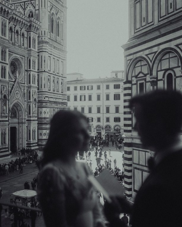A couple standing close in black and white, with the cathedral and bell tower of Florence behind them