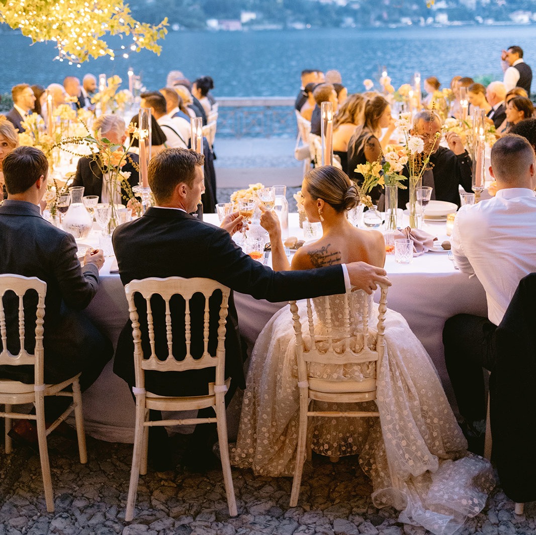 Couple seated at a lakeside reception table with peach florals, Italian Wedding