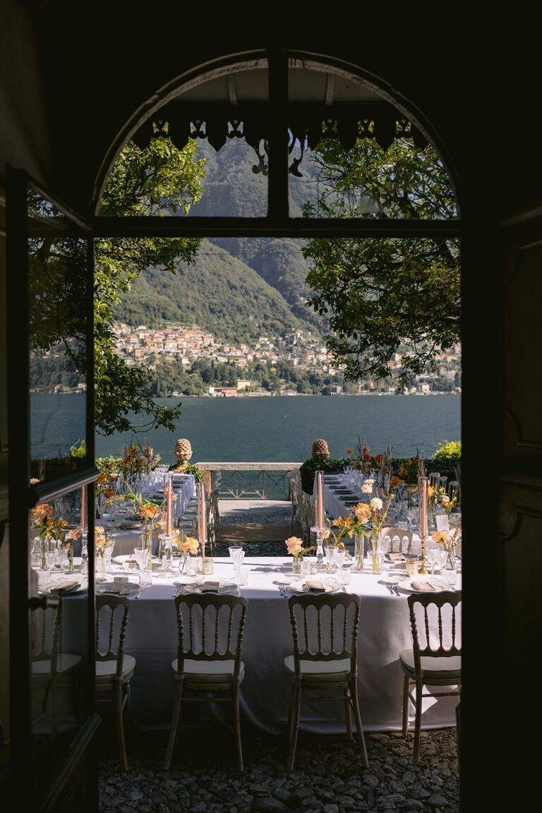 Arched window view over a laid reception table and the lake, Italian Wedding