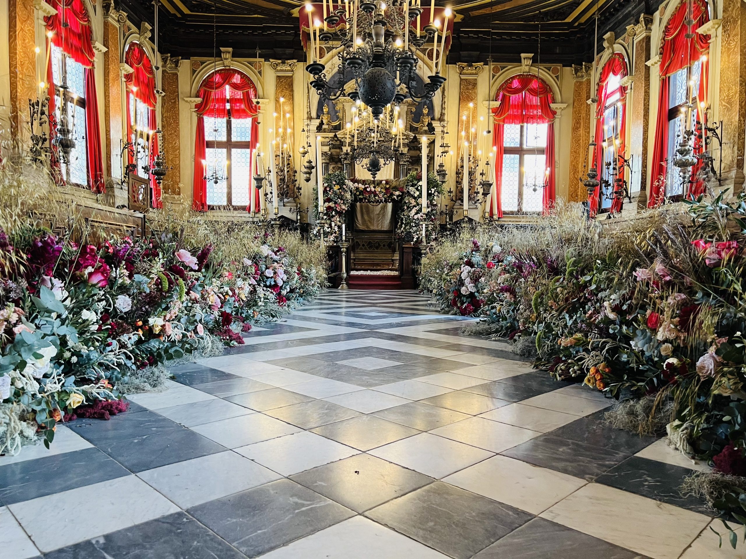 The ceremony aisle runs to a candlelit altar beneath a wrought-iron chandelier, Jamie Aston