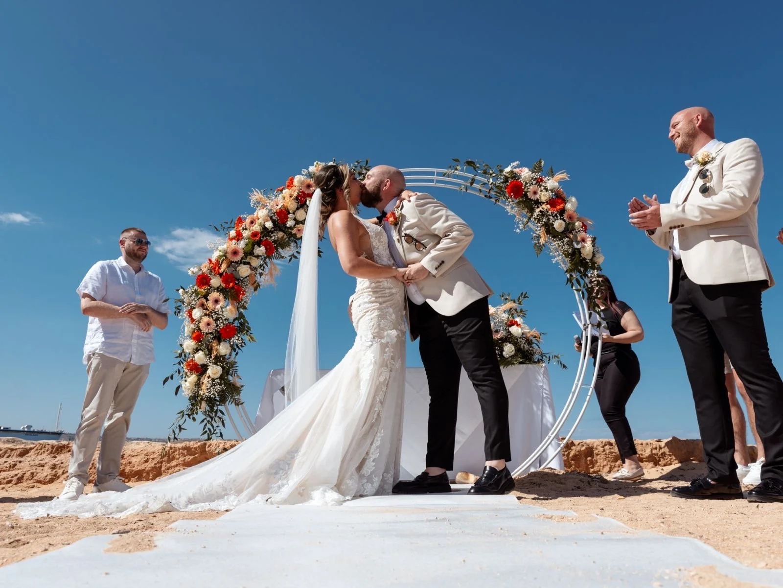 A kiss beneath a floral ceremony arch under a blue Maltese sky, Jewelweddings Event Planners