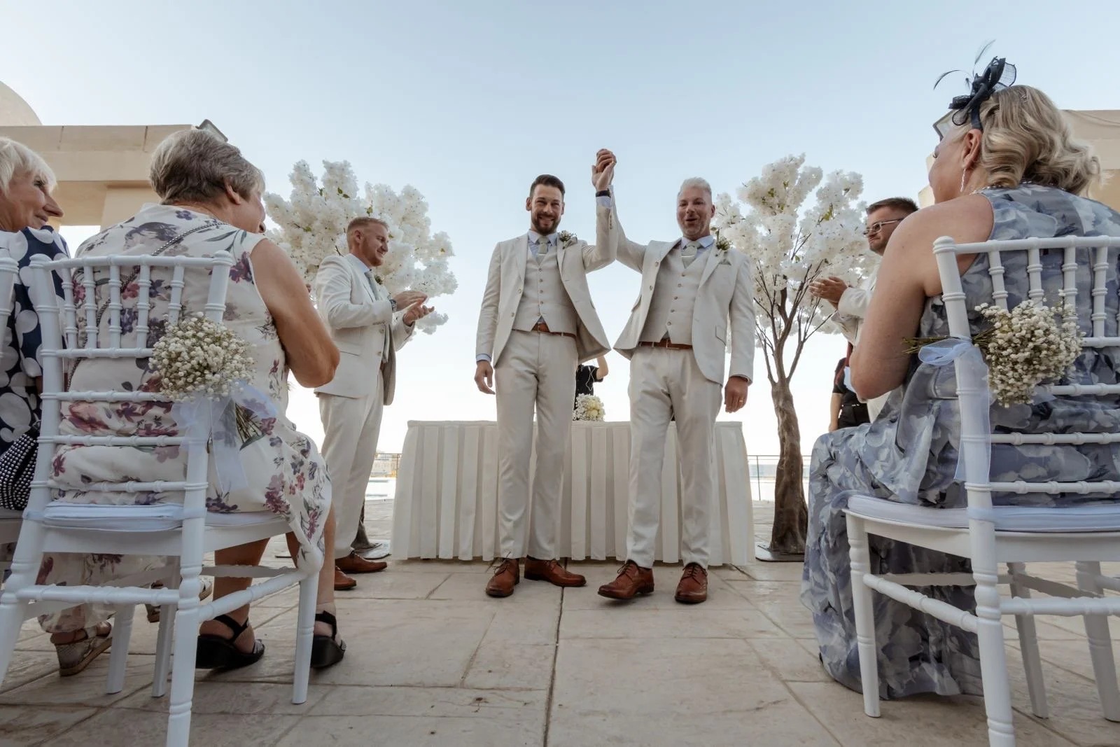 The couple celebrate at the ceremony as guests look on, white floral arrangements behind, Jewelweddings Event Planners