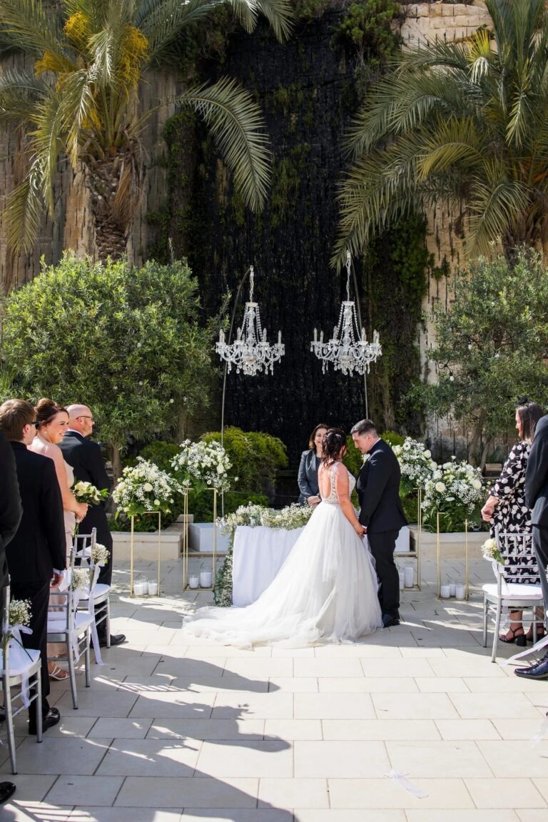 A bride walks a stone path towards a ceremony beneath hanging chandeliers, Jewelweddings Event Planners