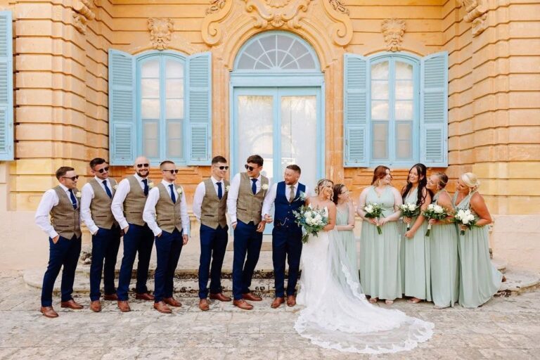 The wedding party lined up before a honey-stone villa with blue shutters, Jewelweddings Event Planners