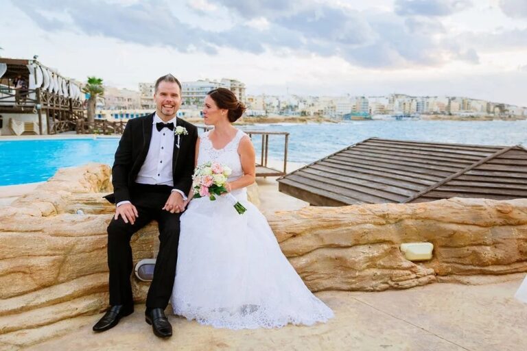 The couple seated on rocks beside a seaside pool terrace at dusk, Jewelweddings Event Planners