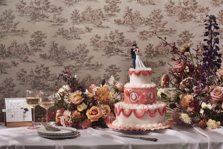Cake with a bride and groom topper among soft pink and lilac flowers on a pink toile backdrop, Jewelweddings Event Planners