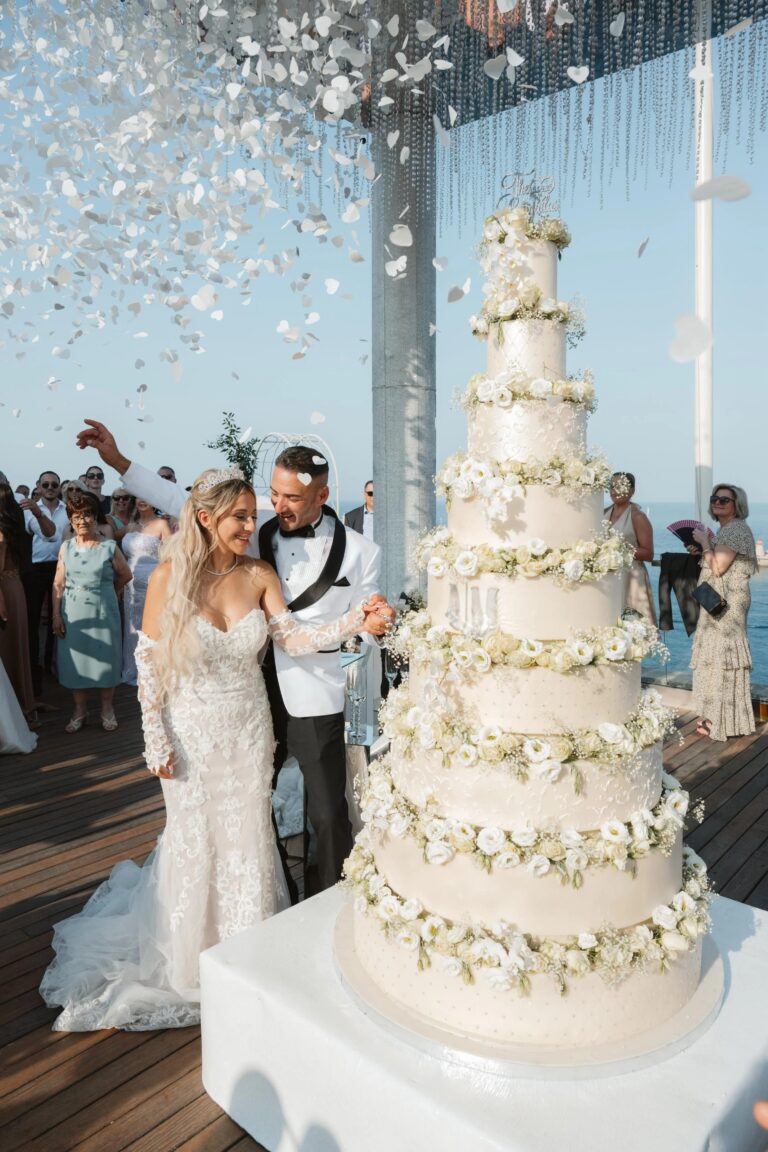 A tall tiered cake dressed with flowers as confetti falls, Jewelweddings Event Planners