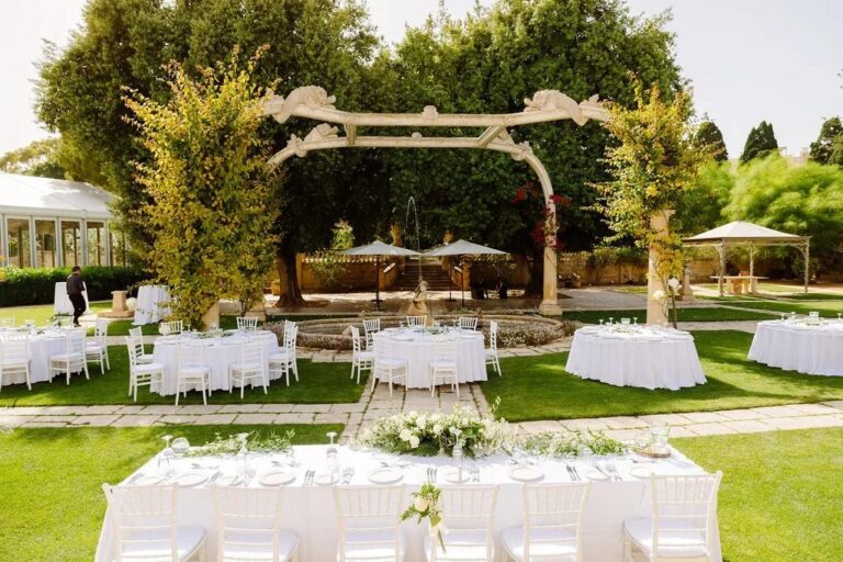 Reception tables laid in a Maltese villa garden beside a stone pergola, Jewelweddings Event Planners