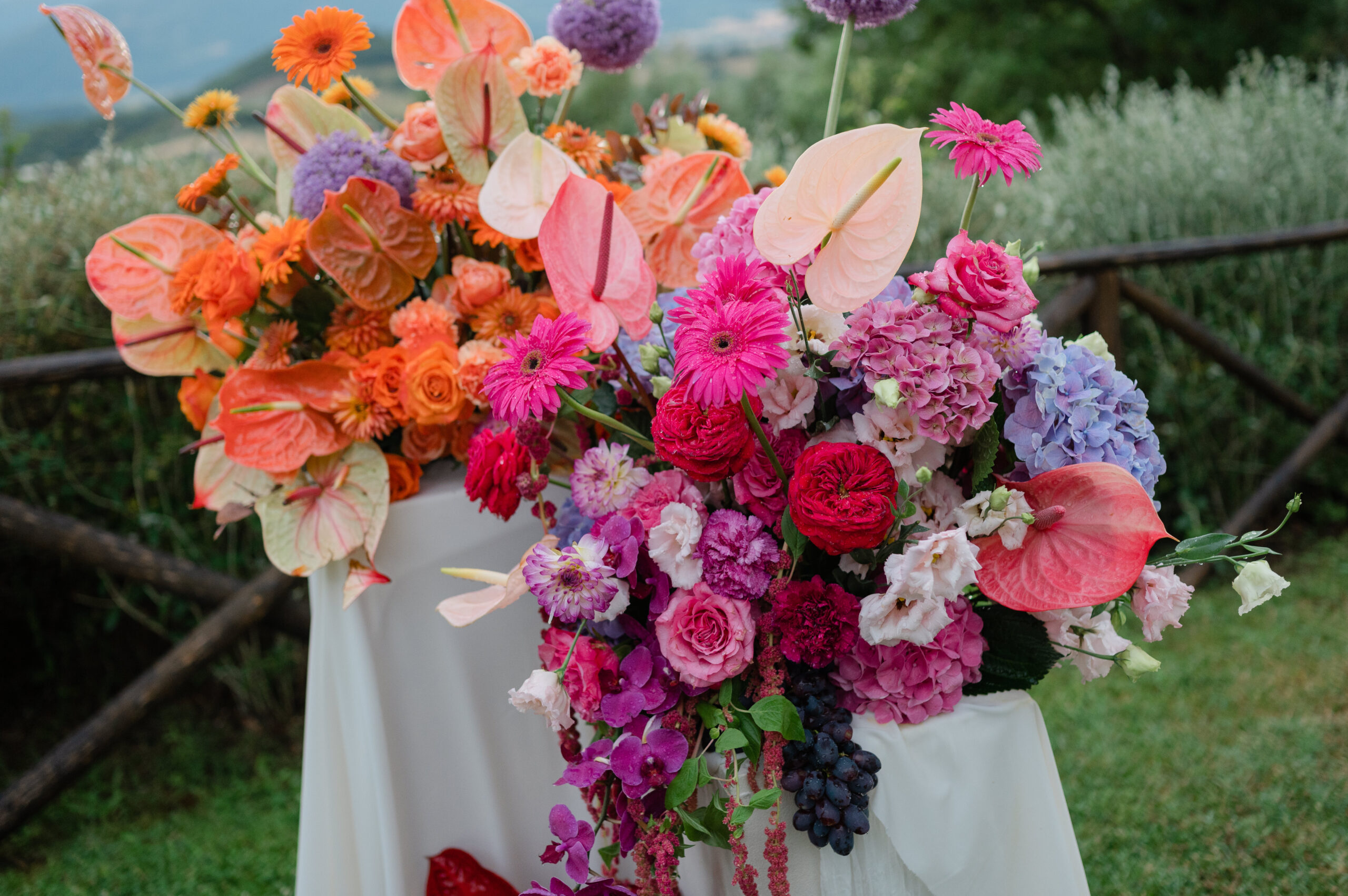 Orange, pink and red ceremony flowers with anthuriums and hydrangeas on a draped plinth at Nikis Resort, Umbria, Joy Wedding