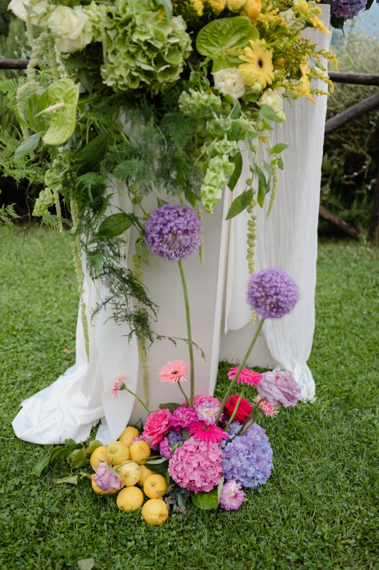 A draped ceremony pillar with hydrangeas, alliums and lemons at its base, Nikis Resort, Umbria, Joy Wedding