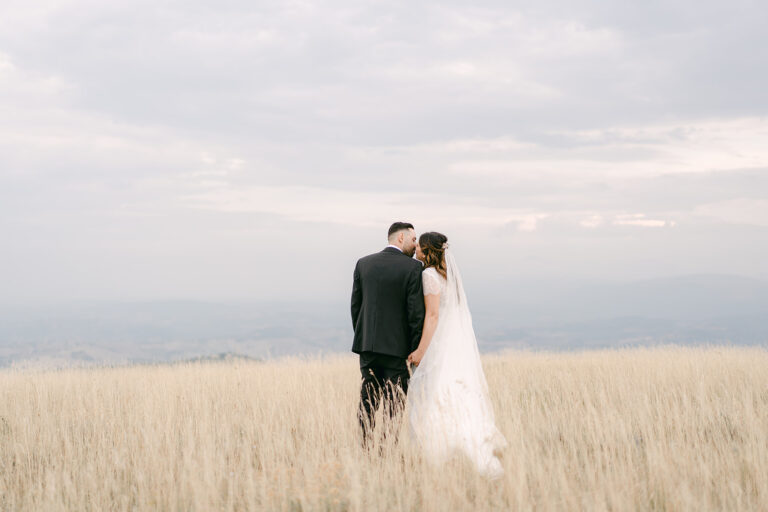 A couple in a field of dry grass above the Marche hills, from a wedding at Villa Nena, Tolentino, Joy Wedding