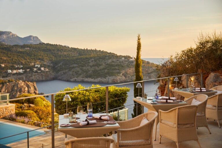A clifftop restaurant terrace, tables set above the cove and a single cypress tree, Jumeirah Port Soller Hotel & Spa