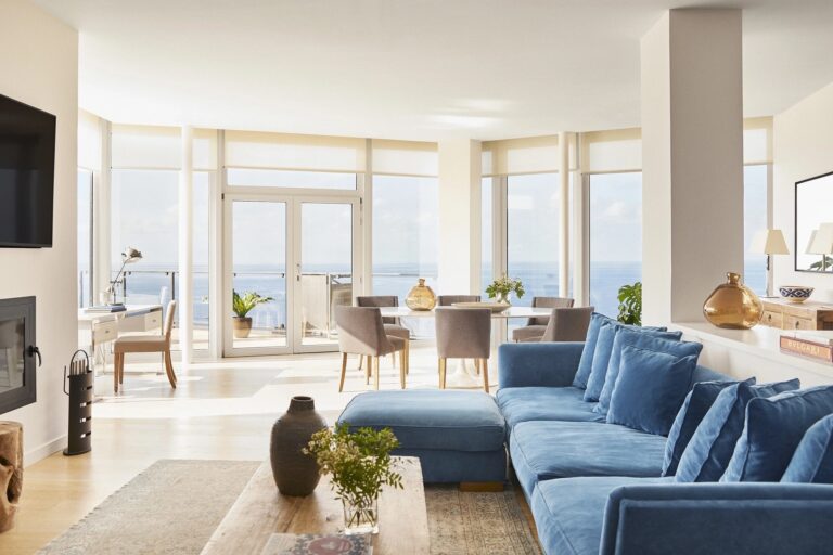 A bright suite living room with blue sofas and a view to the water, Jumeirah Port Soller Hotel & Spa
