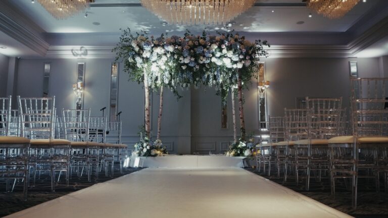 Chuppah and white aisle runner beneath a floral canopy in a hotel ceremony room, Just Smile Ltd