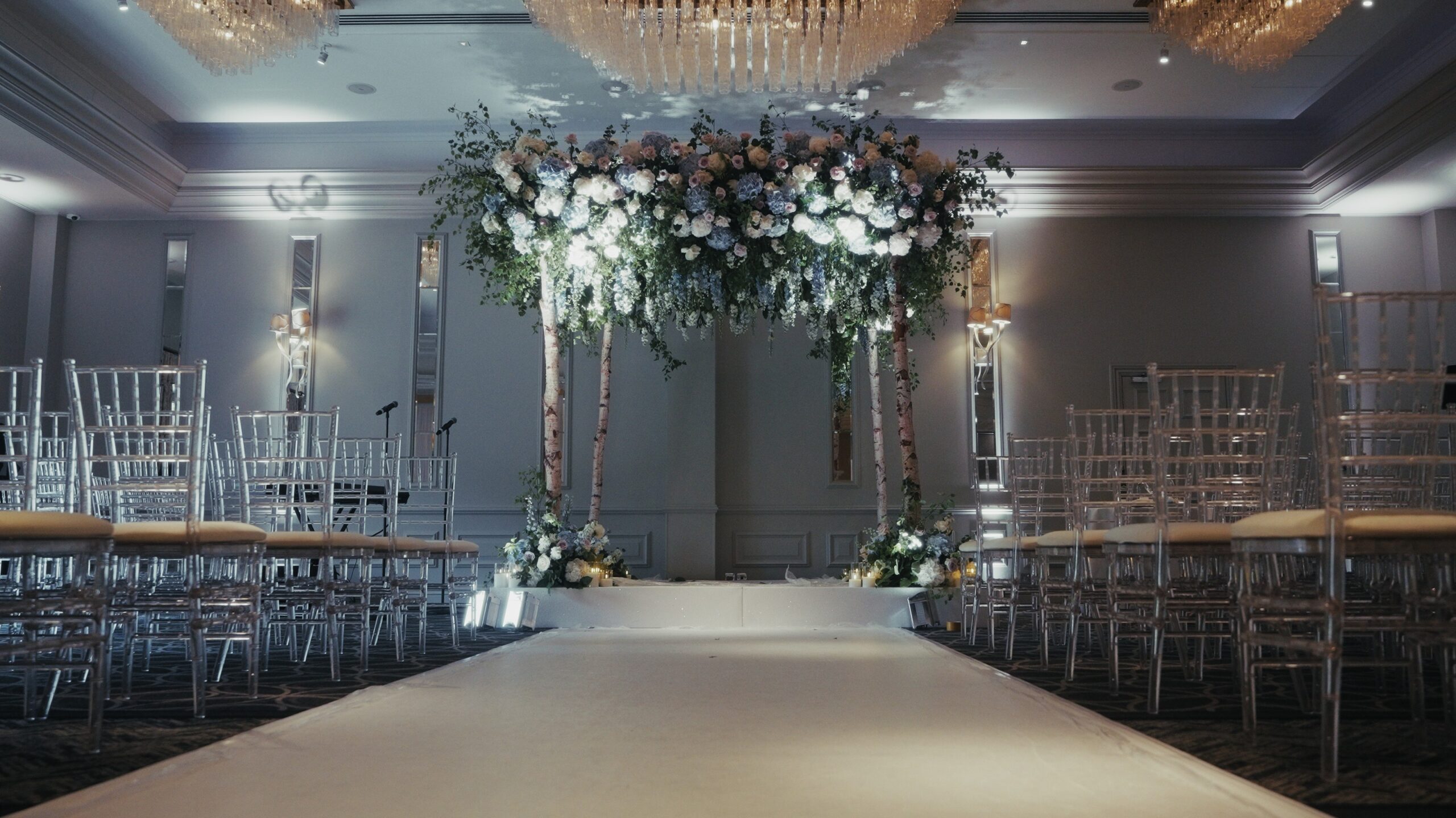 Chuppah and white aisle runner beneath a floral canopy in a hotel ceremony room, Just Smile Ltd