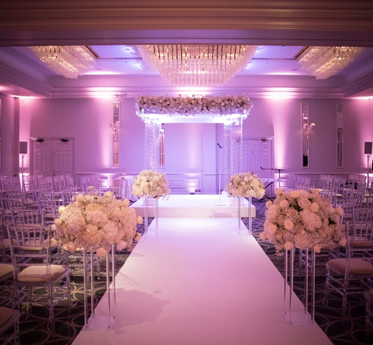 White aisle runner leading to an uplit chuppah with flower arrangements, Just Smile Ltd