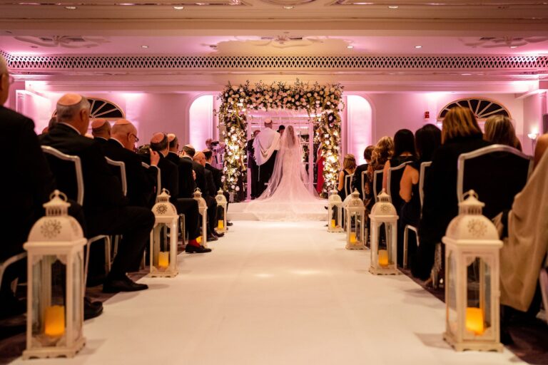 Lantern-lined aisle toward a floral chuppah with guests seated, Just Smile Ltd