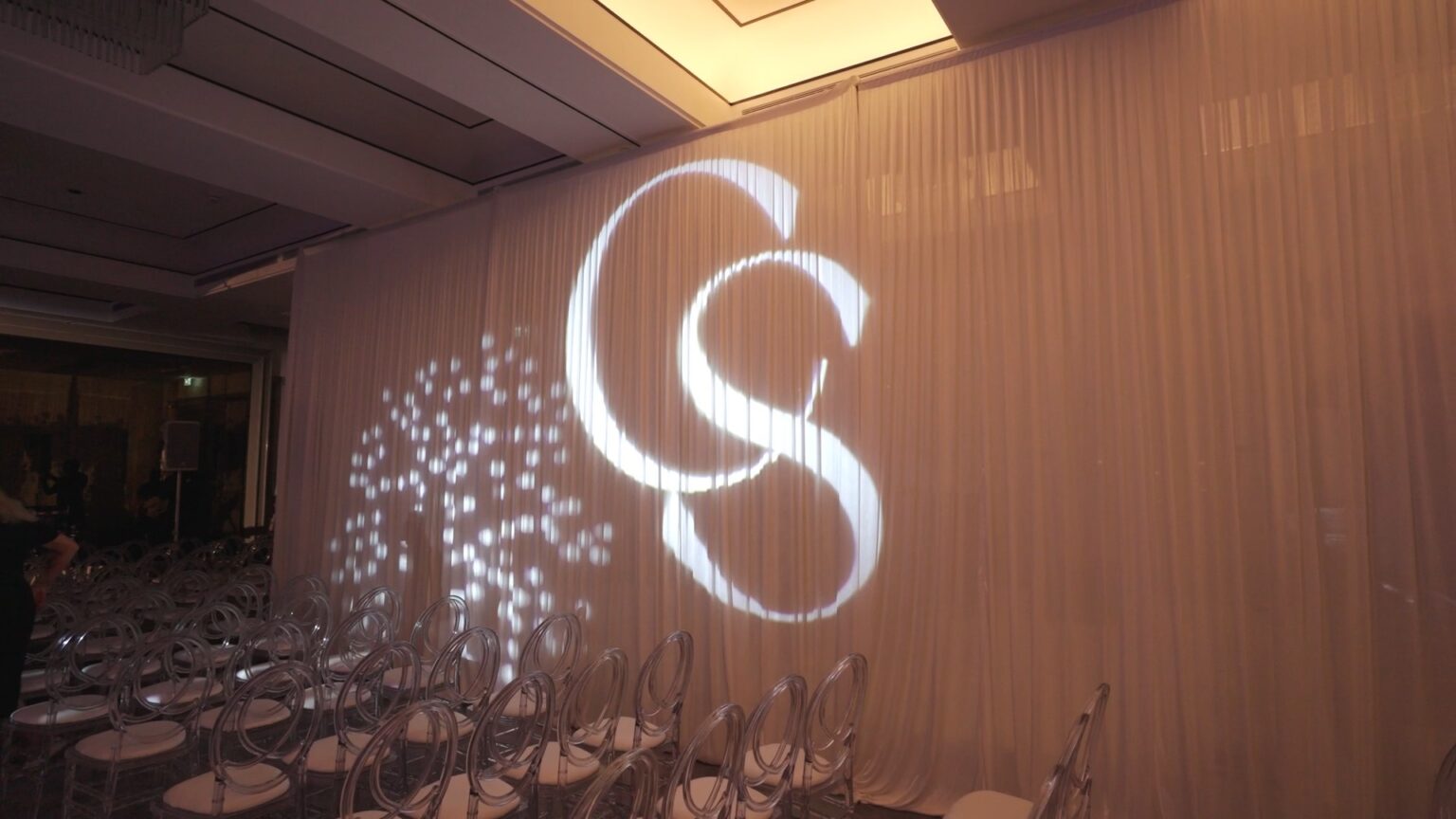 A monogram projected onto a white silk backdrop behind the ceremony seating