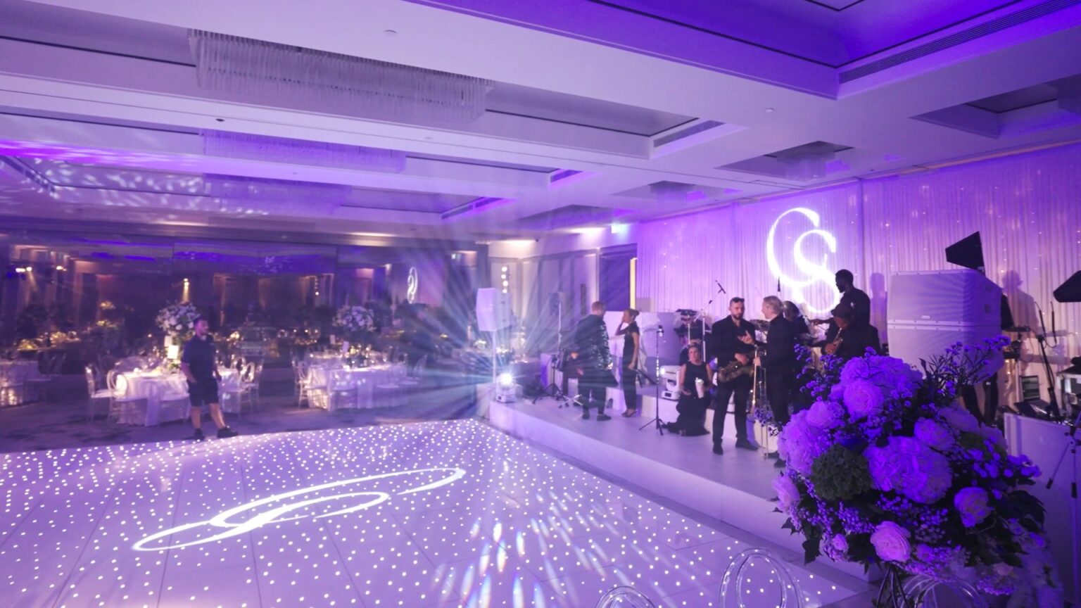 A starlit white dance floor with a projected monogram and purple uplighting