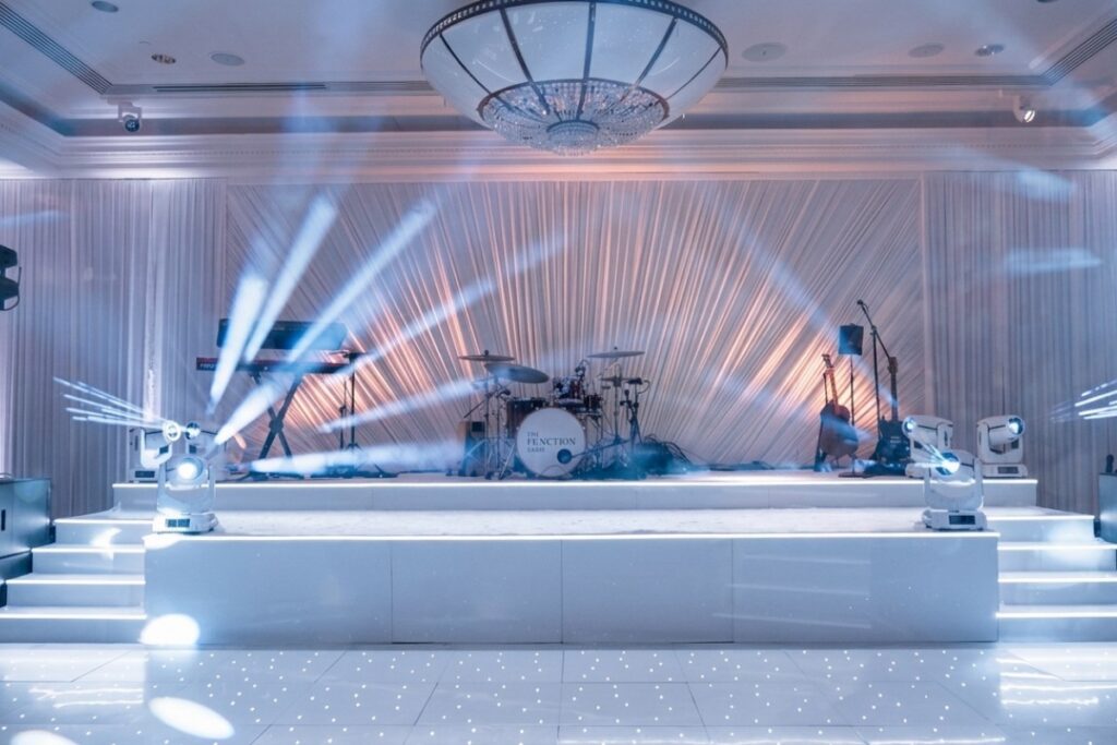 Carpeted white stage with moving heads, drum kit and uplit drapes, Just Smile Ltd