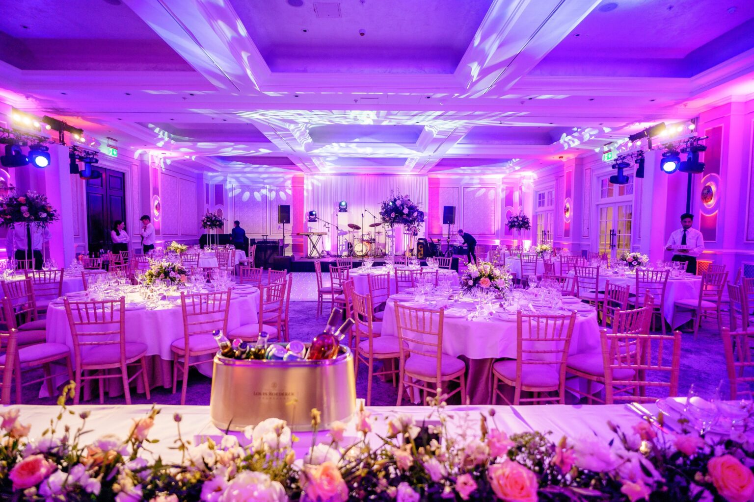 A ballroom reception in magenta uplighting with a floral sweetheart table