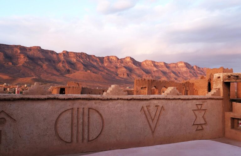 Kasbah rooftop wall with carved Amazigh symbols and mountain ridge at sunset, Kasbah des Caïds