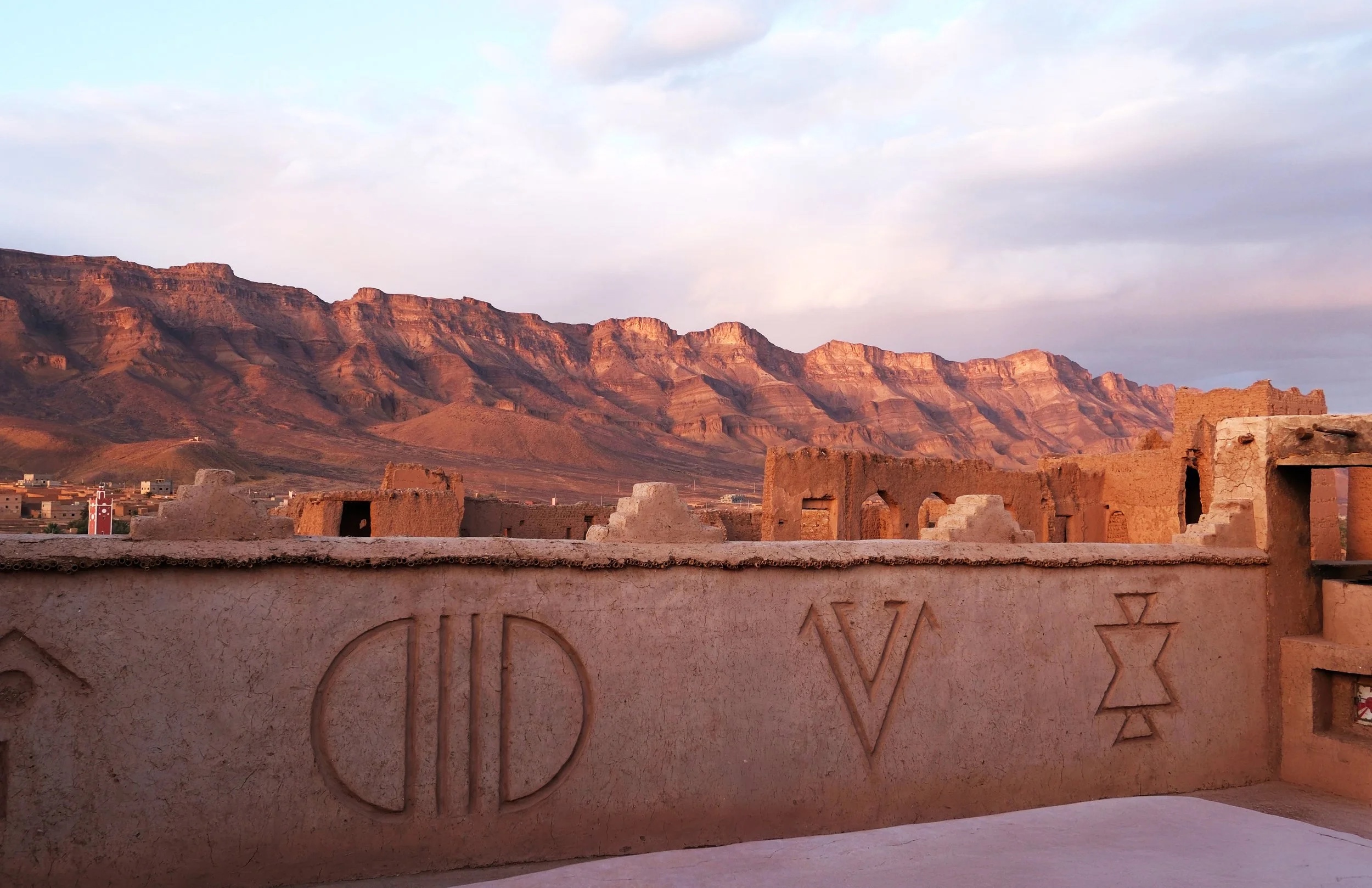 Kasbah rooftop wall with carved Amazigh symbols and mountain ridge at sunset, Kasbah des Caïds