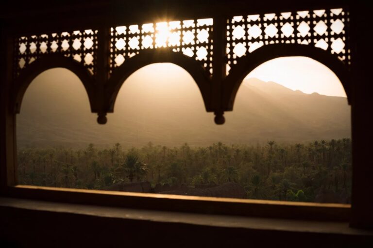 Palm oasis seen through carved window arches at sunset, Kasbah des Caïds