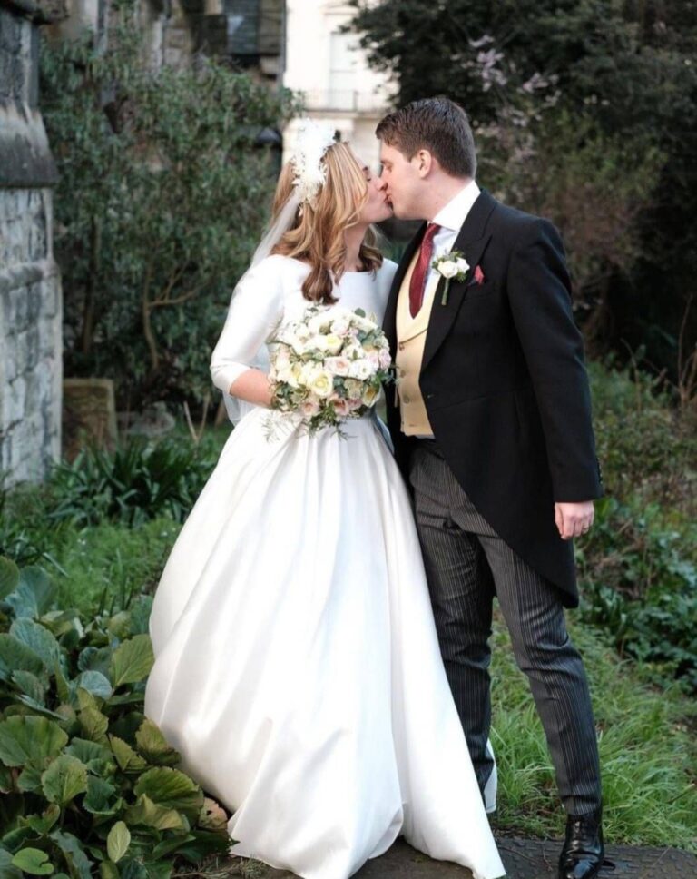 A bride in a full skirted gown kissing her groom on the lawn, Kate Edmondson Bridal Couture