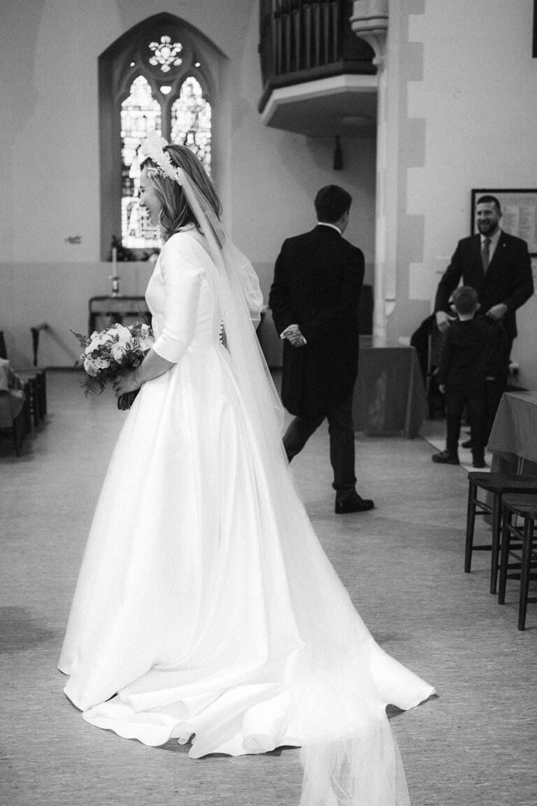 A bride in a long veil and full skirted gown inside a church, in black and white, Kate Edmondson Bridal Couture
