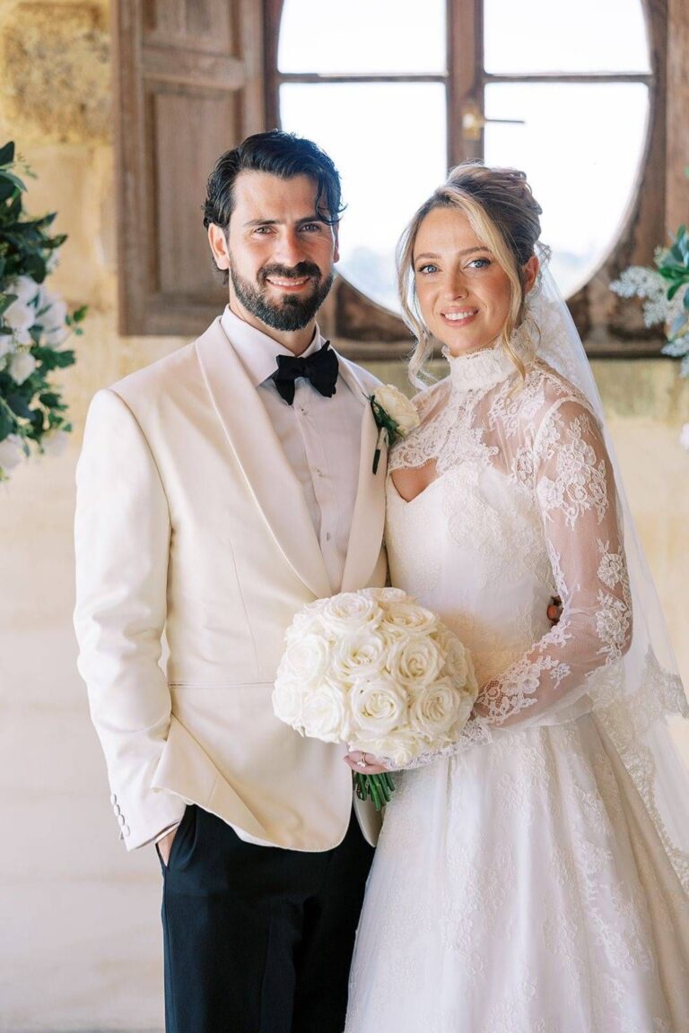 A bride in a lace sleeved gown beside her groom in a white dinner jacket, Kate Edmondson Bridal Couture