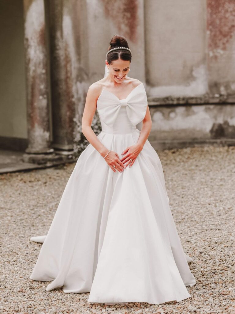 A ball gown with a bow at the bodice on a gravel drive, Kate Edmondson Bridal Couture