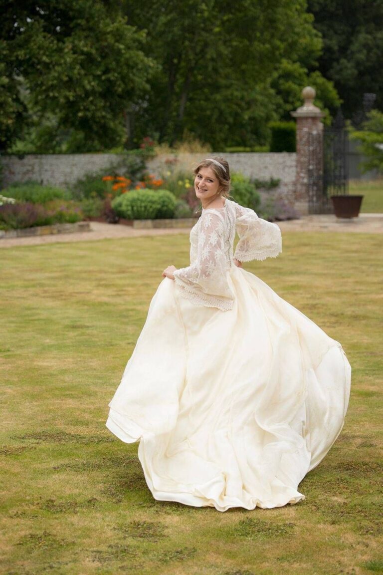 A bride in a lace sleeved gown twirling on a lawn, Kate Edmondson Bridal Couture