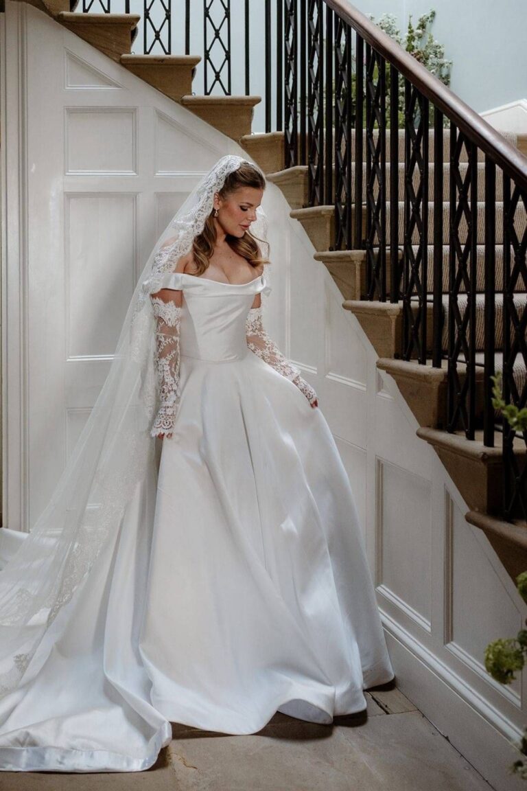 A bride in an off shoulder gown and long veil on a staircase, Kate Edmondson Bridal Couture