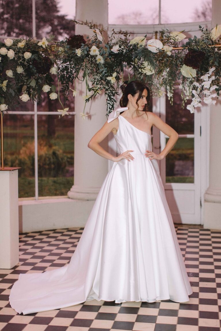 A one shoulder satin gown with a long train beneath hanging flowers, Kate Edmondson Bridal Couture