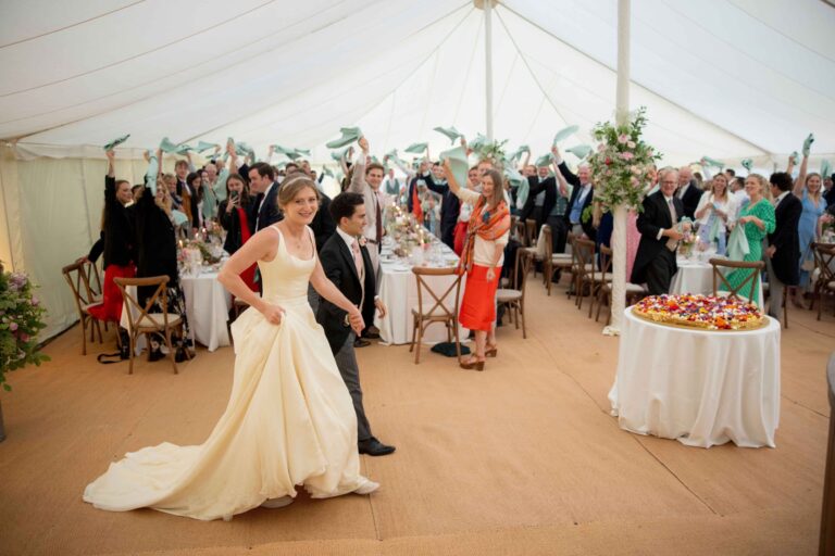 A bride in a full skirted ivory gown walking through a marquee reception, Kate Edmondson Bridal Couture