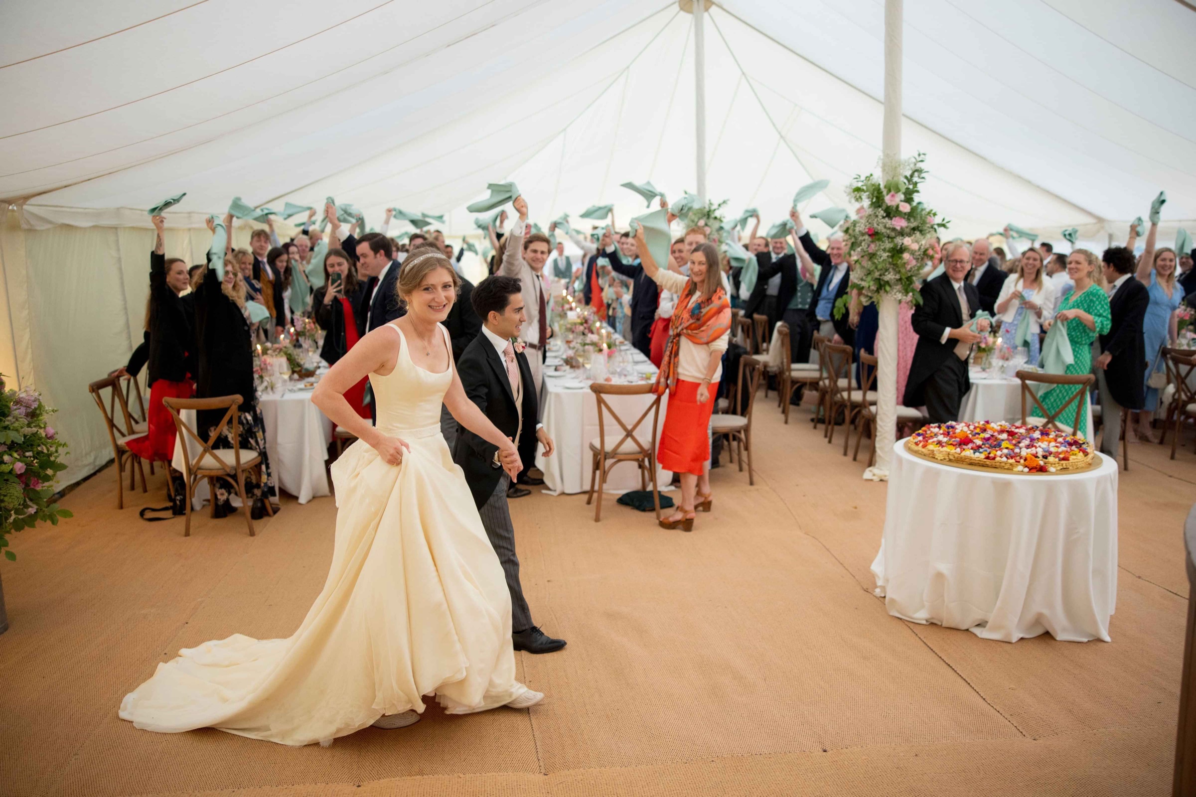 A bride in a full skirted ivory gown walking through a marquee reception, Kate Edmondson Bridal Couture