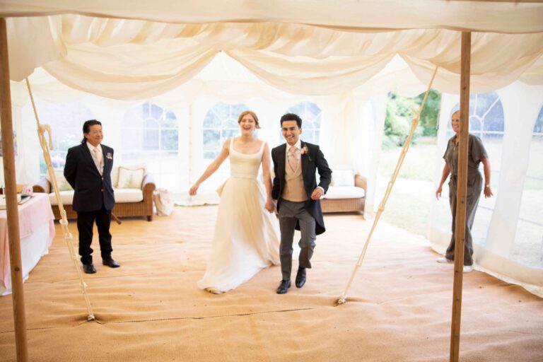 A bride in a long gown and her groom crossing a draped marquee, Kate Edmondson Bridal Couture