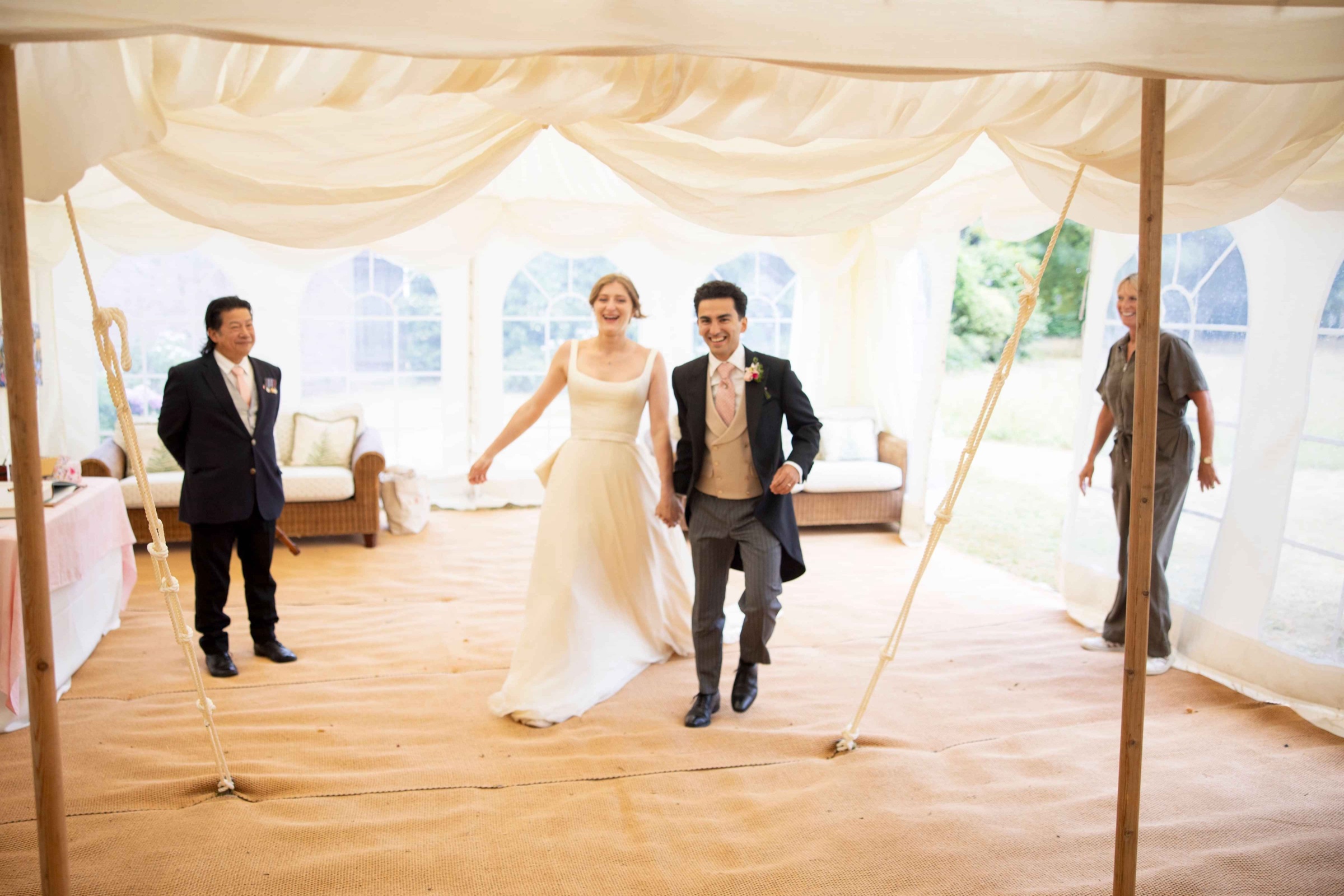A bride in a long gown and her groom crossing a draped marquee, Kate Edmondson Bridal Couture