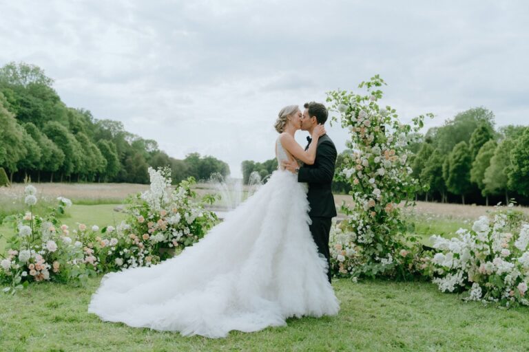 Couple kissing among tall clusters of white and blush flowers on the lawn, Katerina Meyvial Wedding & Event Planner