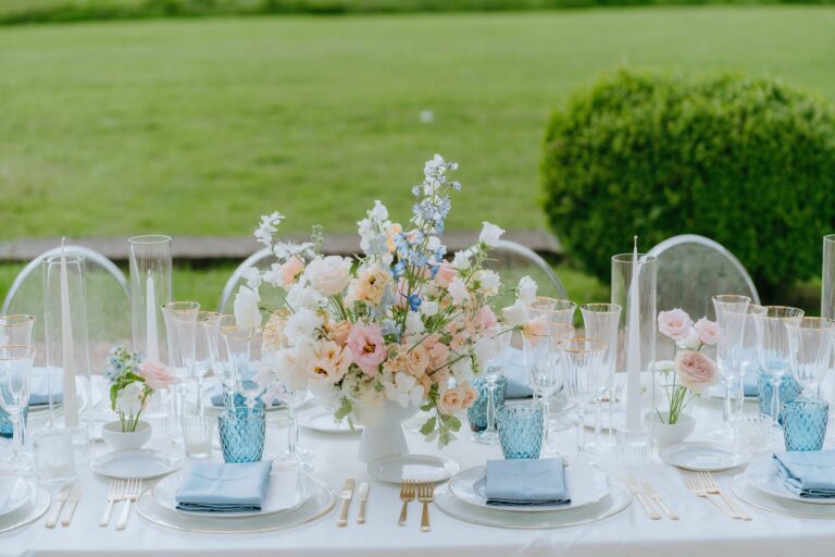 Table detail with pastel florals, blue glasses and acrylic chairs on the grass, Katerina Meyvial Wedding & Event Planner