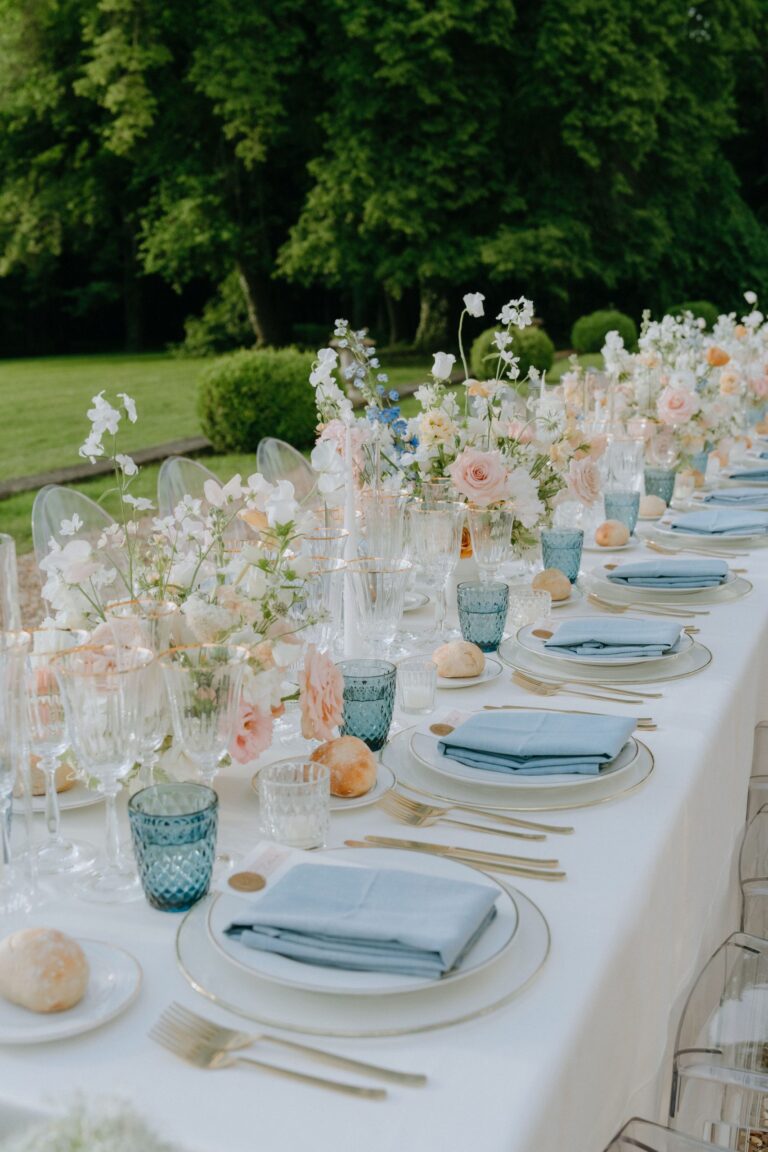 Garden banquet table set in blue and peach beneath tall trees, Katerina Meyvial Wedding & Event Planner