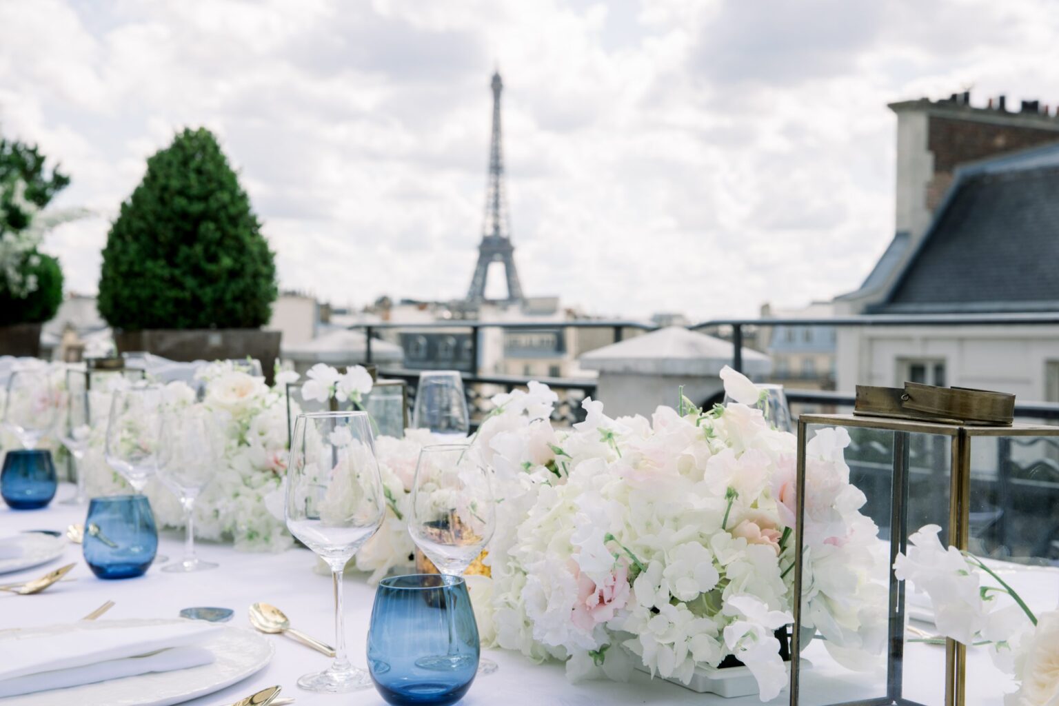 A rooftop table dressed in white flowers and blue glass, the Eiffel Tower in the distance