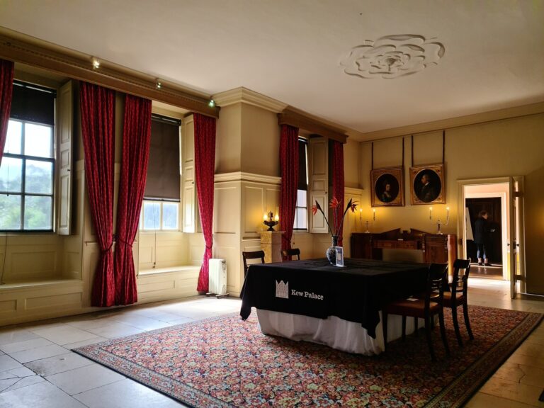 A State Room set for an intimate wedding breakfast, red silk curtains at the tall windows, Kew Palace