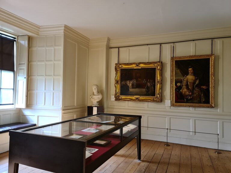 A panelled room hung with royal portraits, a case of relics at its centre, Kew Palace