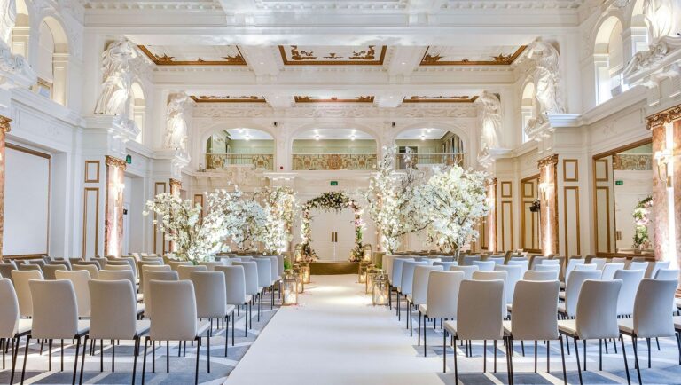 The Ballroom set for a ceremony, with rows of chairs either side of a white aisle and blossom trees along the walls, Kimpton Fitzroy London