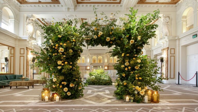 A freestanding archway of greenery and yellow roses in the Ballroom, with candles at its base, Kimpton Fitzroy London