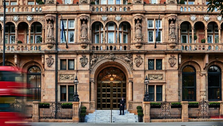 The terracotta Victorian facade on Russell Square, with the arched main entrance, carved stonework and a doorman on the steps, Kimpton Fitzroy London