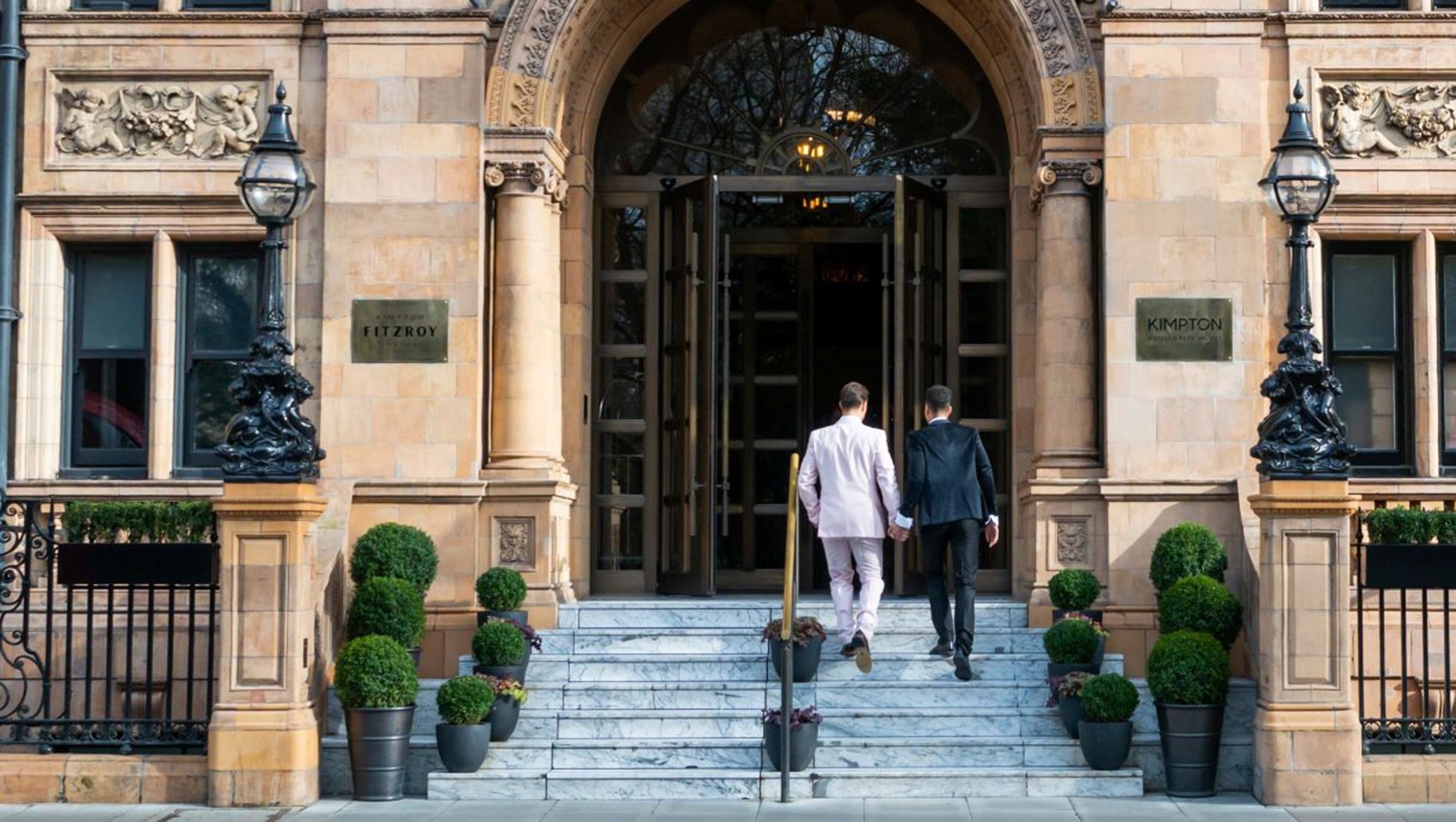 The arched main entrance, flanked by lanterns and clipped box, with two guests climbing the steps, Kimpton Fitzroy London